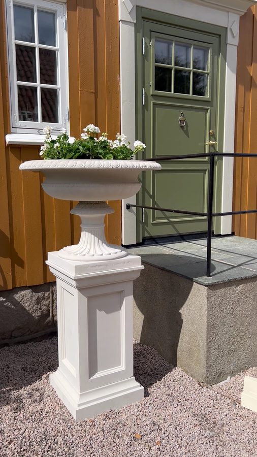 Hvit urne på høy pidestall ved inngangsdøren til villaen