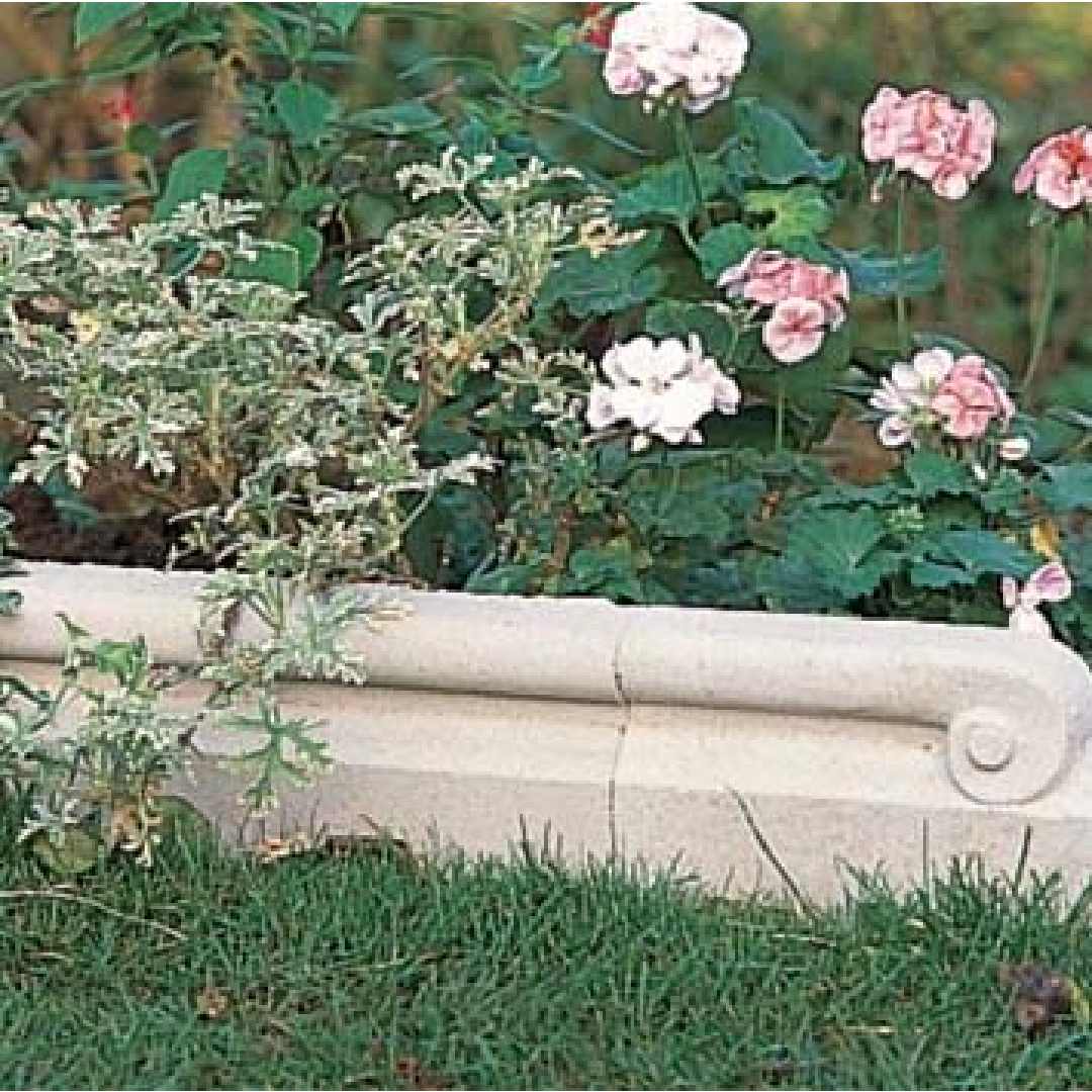 Ornamentert kantstein i støpt stein langs et blomstrende bed