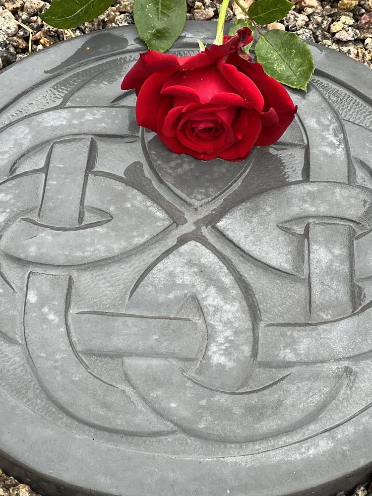 Rød rose lagt på en tråkkhelle med hugget keltisk knutemønster